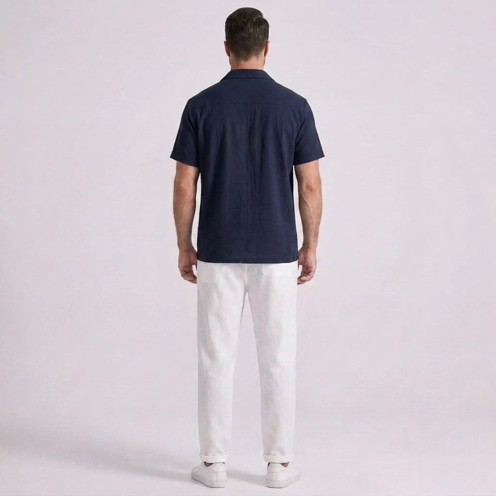 Man wearing a navy blue polo shirt and white pants on a light gray background