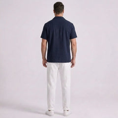 Man wearing a navy blue polo shirt and white pants on a light gray background