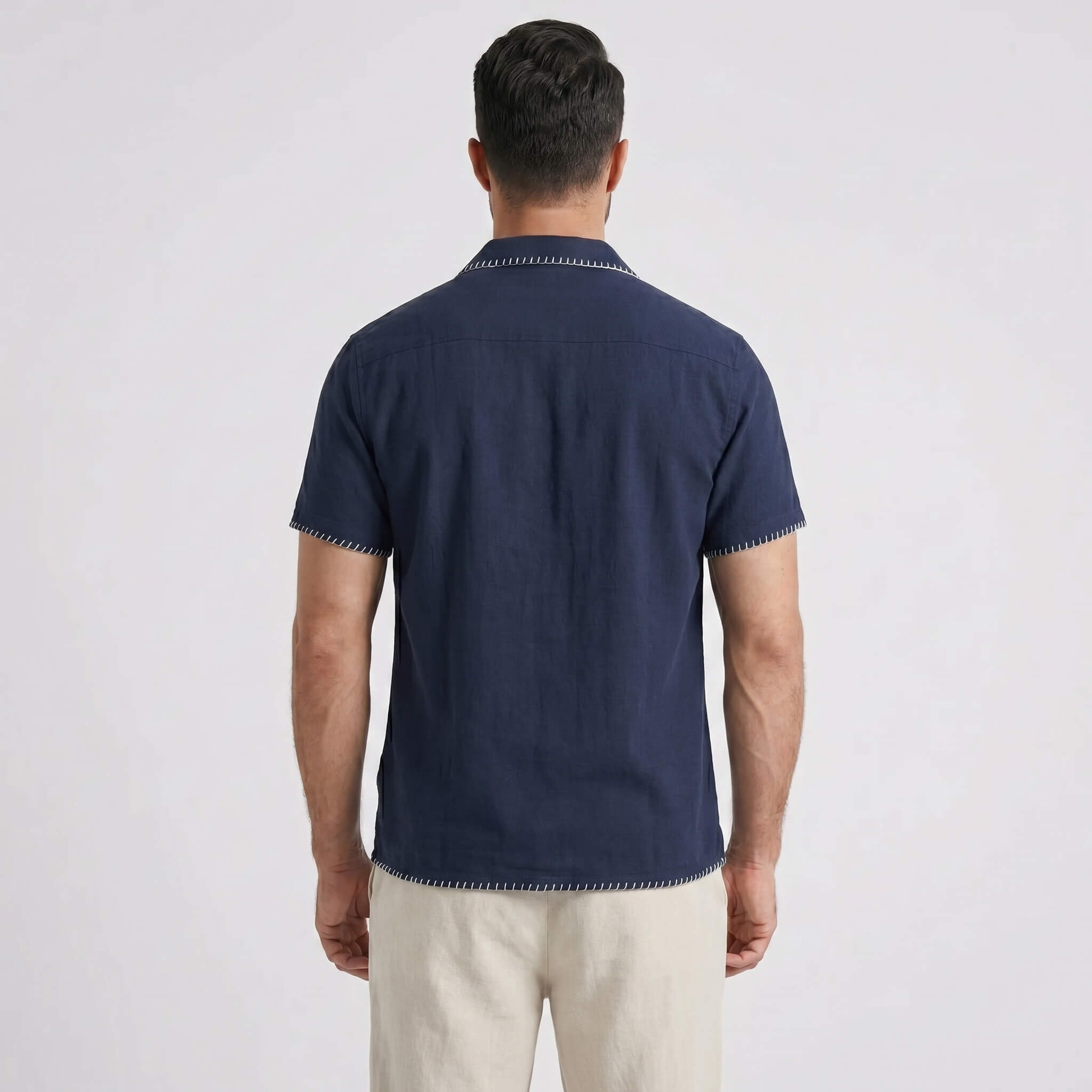 Man wearing a navy blue polo shirt with white pants on a light gray background