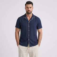 Man wearing a navy blue short-sleeve shirt with white pants on a light gray background