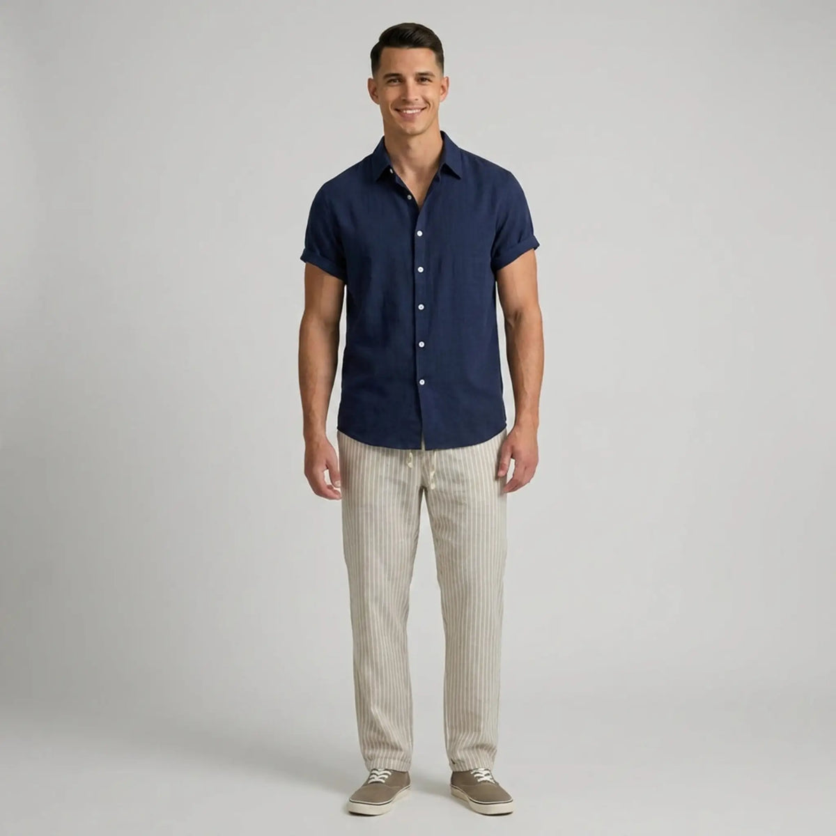Man wearing a navy button-up shirt and beige striped pants on a gray background