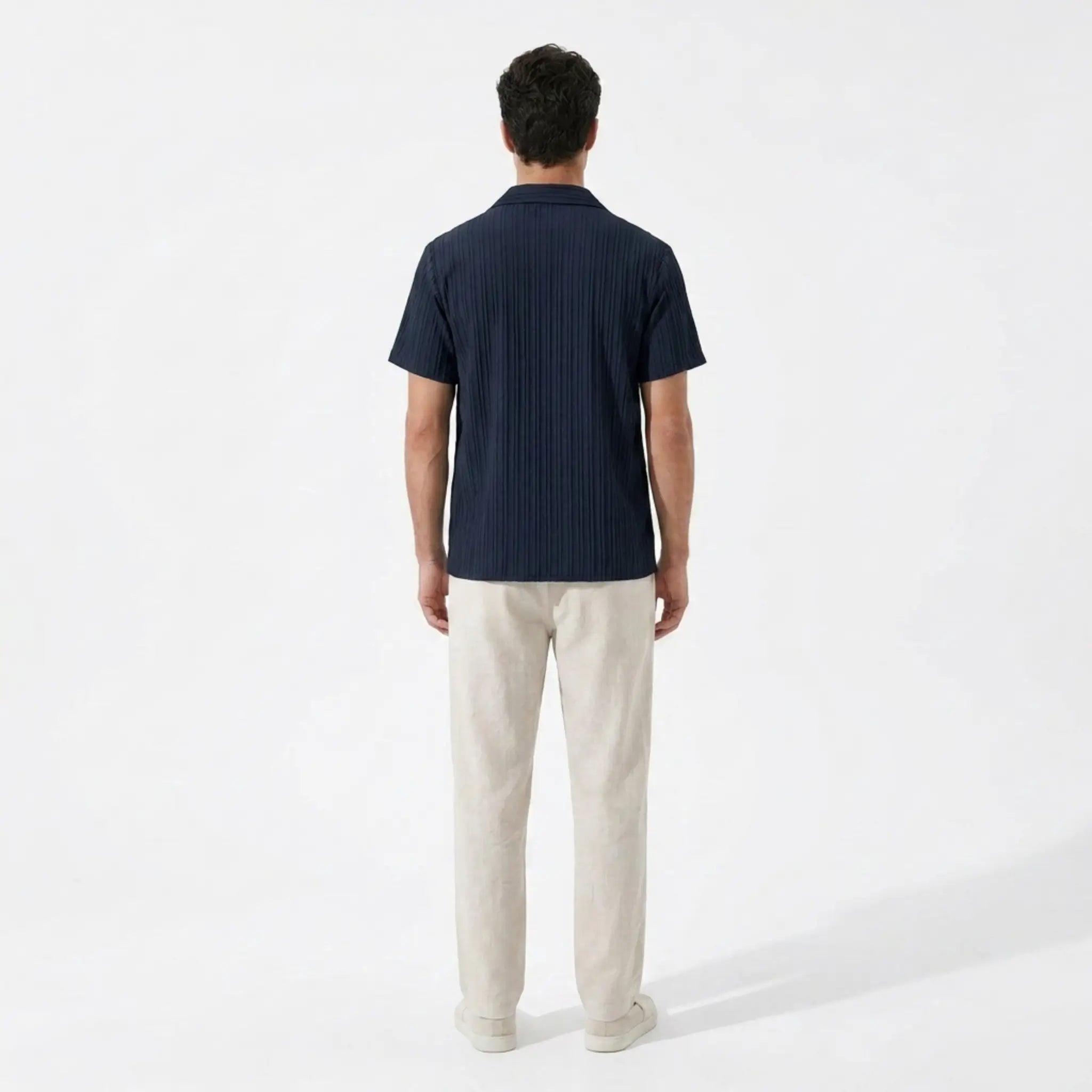 Man wearing a navy polo shirt and beige pants on a white background