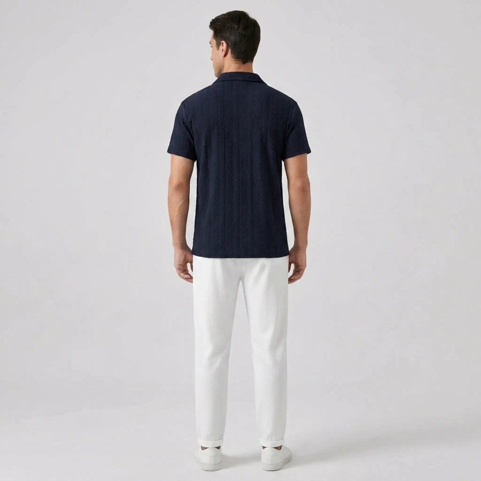 Man wearing a navy polo shirt and white pants  back view on a light gray background