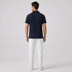 Man wearing a navy polo shirt and white pants  back view on a light gray background