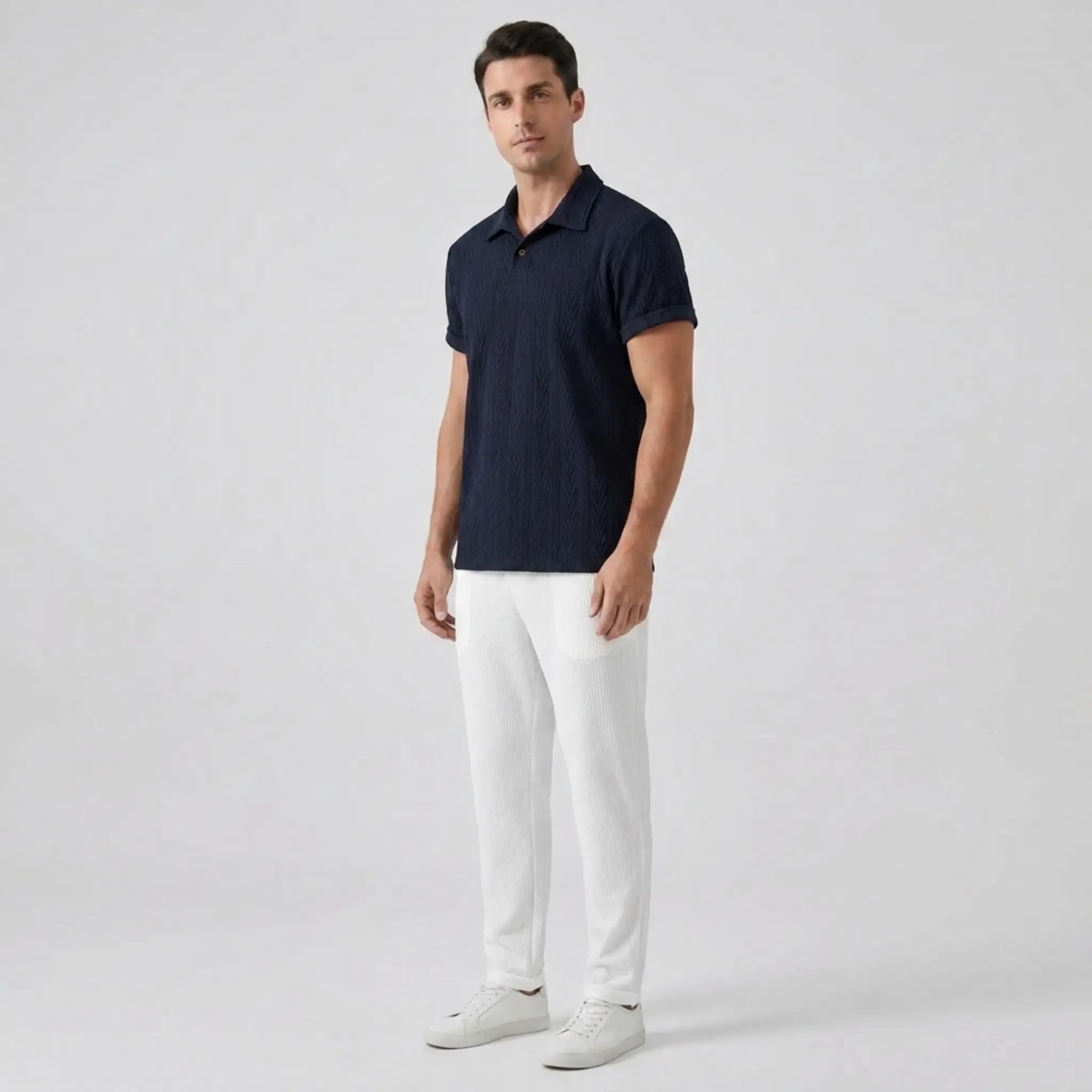 Man wearing a navy polo shirt and white pants on a light gray background