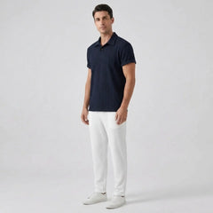 Man wearing a navy polo shirt and white pants on a light gray background