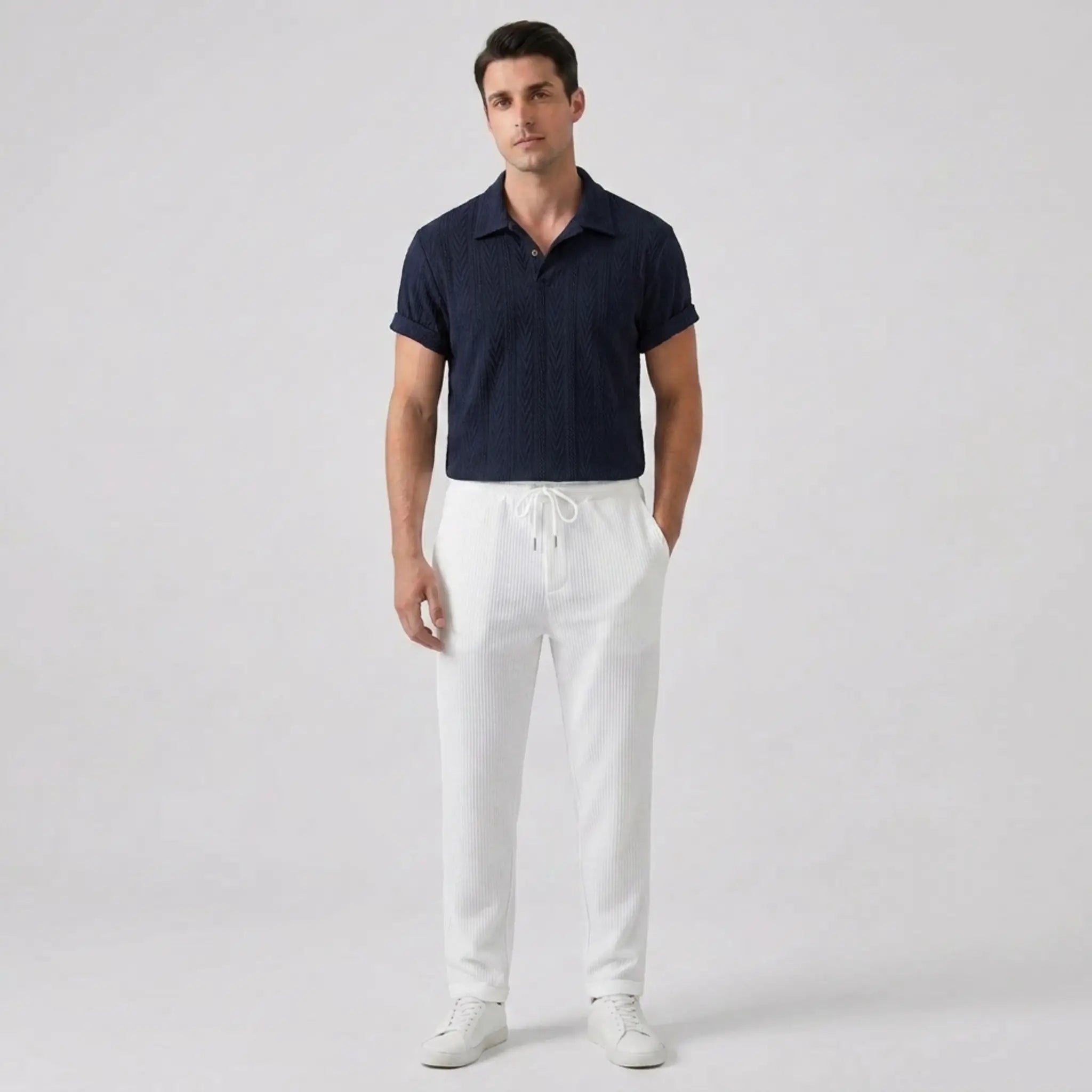 Man wearing a navy polo shirt and white pants on a light gray background