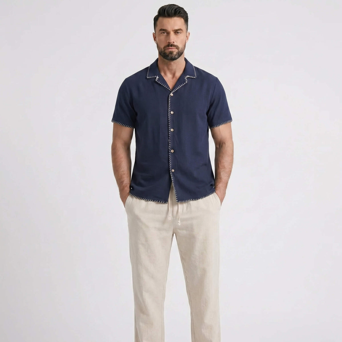 Man wearing a navy short-sleeve shirt and beige pants on a white background