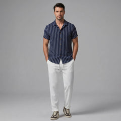 Man wearing a navy striped shirt and white pants on a gray background