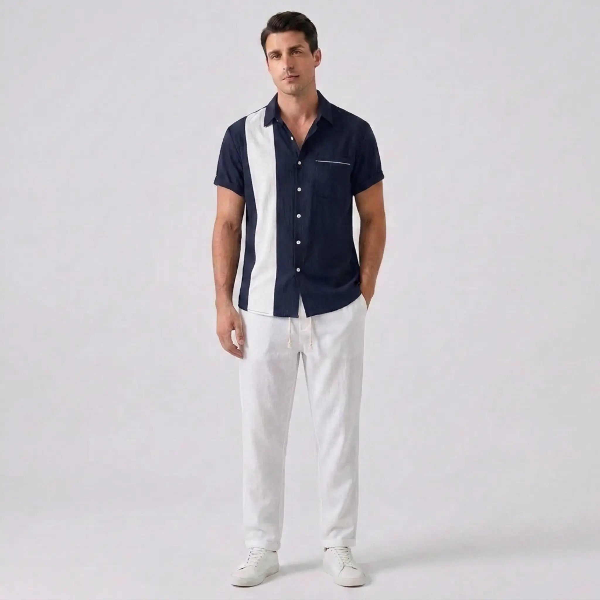 Man wearing a navy and white button-up shirt with white pants on a light gray background