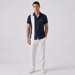 Man wearing a navy and white button-up shirt with white pants on a light gray background