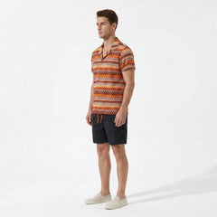 Man wearing a patterned orange and brown shirt with black shorts on a white background