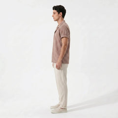 Man wearing a patterned tan shirt and beige pants on a white background