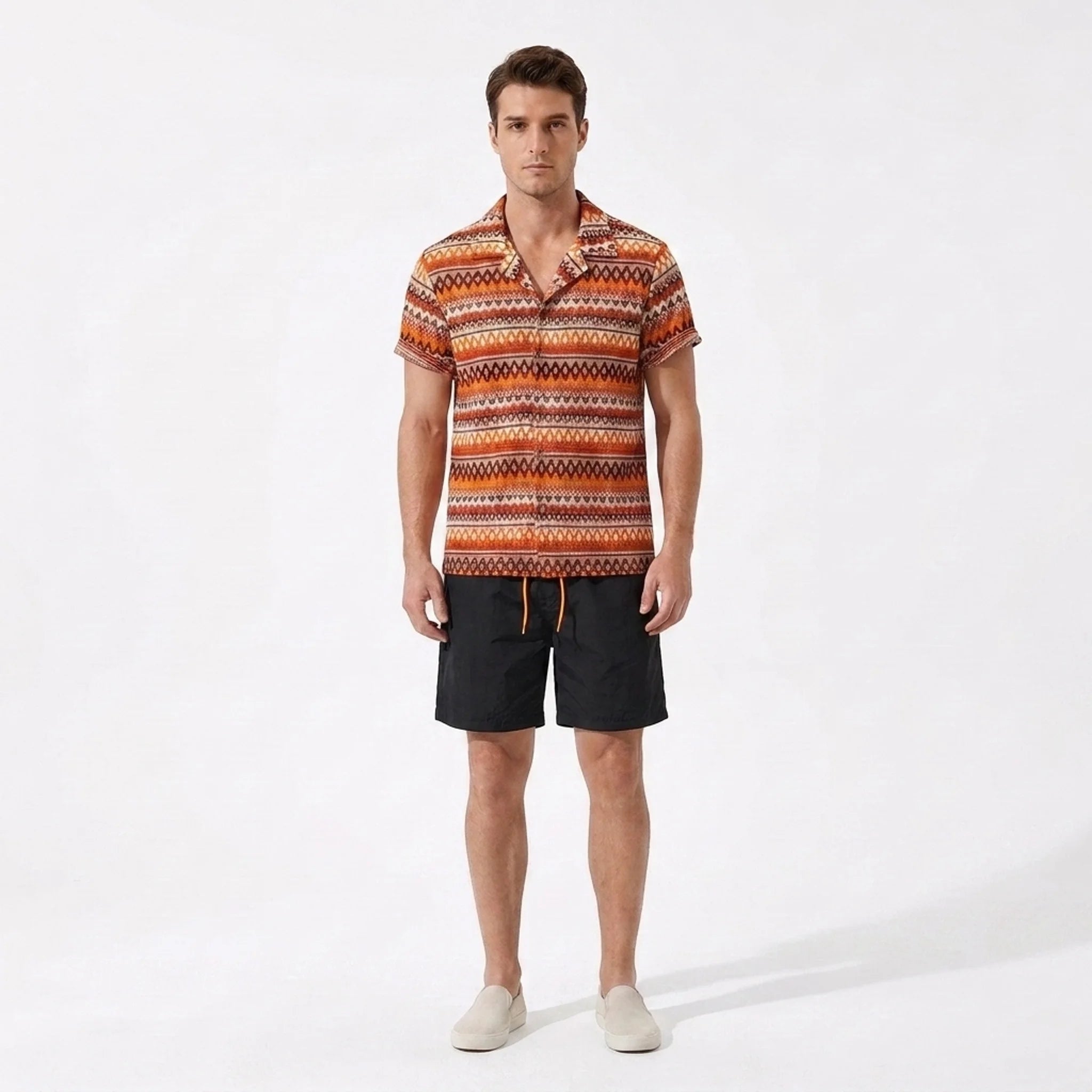 Man wearing a patterned shirt and black shorts on a white background