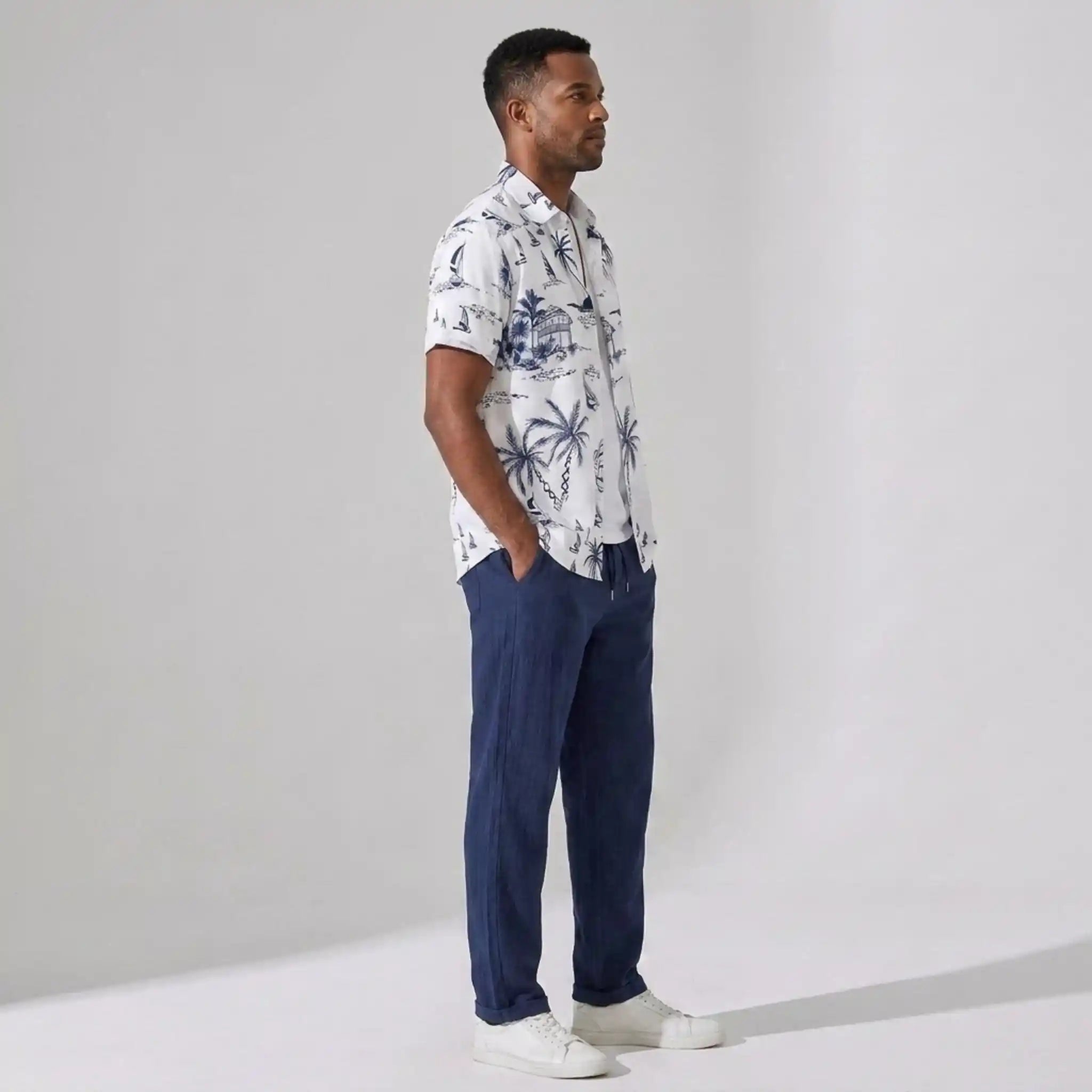 Man wearing a patterned shirt and navy pants against a plain background
