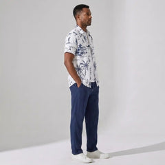 Man wearing a patterned shirt and navy pants against a plain background