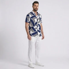 Man wearing a patterned shirt and white pants on a light gray background