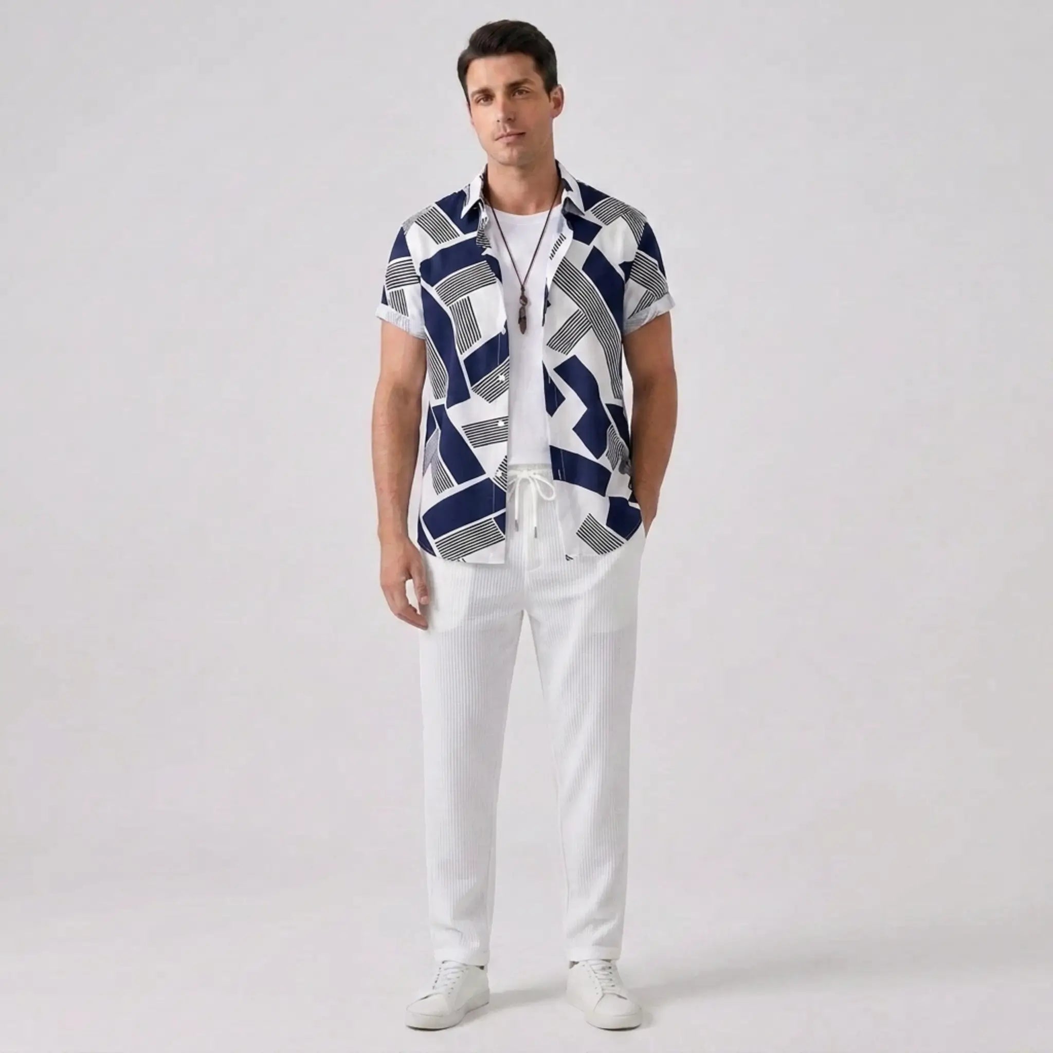 Man wearing a patterned shirt and white pants on a plain background