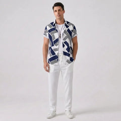 Man wearing a patterned shirt and white pants on a plain background