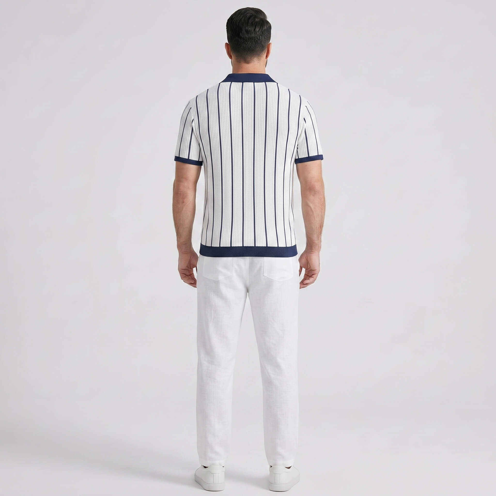 Man wearing a striped polo shirt and white pants on a light gray background