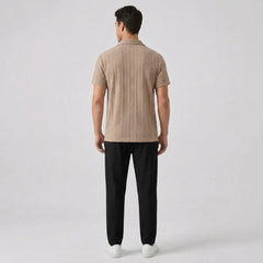 Man wearing a tan knitted polo shirt and black pants back view on a light gray background