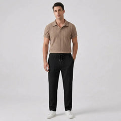 Man wearing a tan polo shirt and black pants on a light gray background