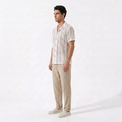 Man wearing a white patterned shirt and beige pants on a white background