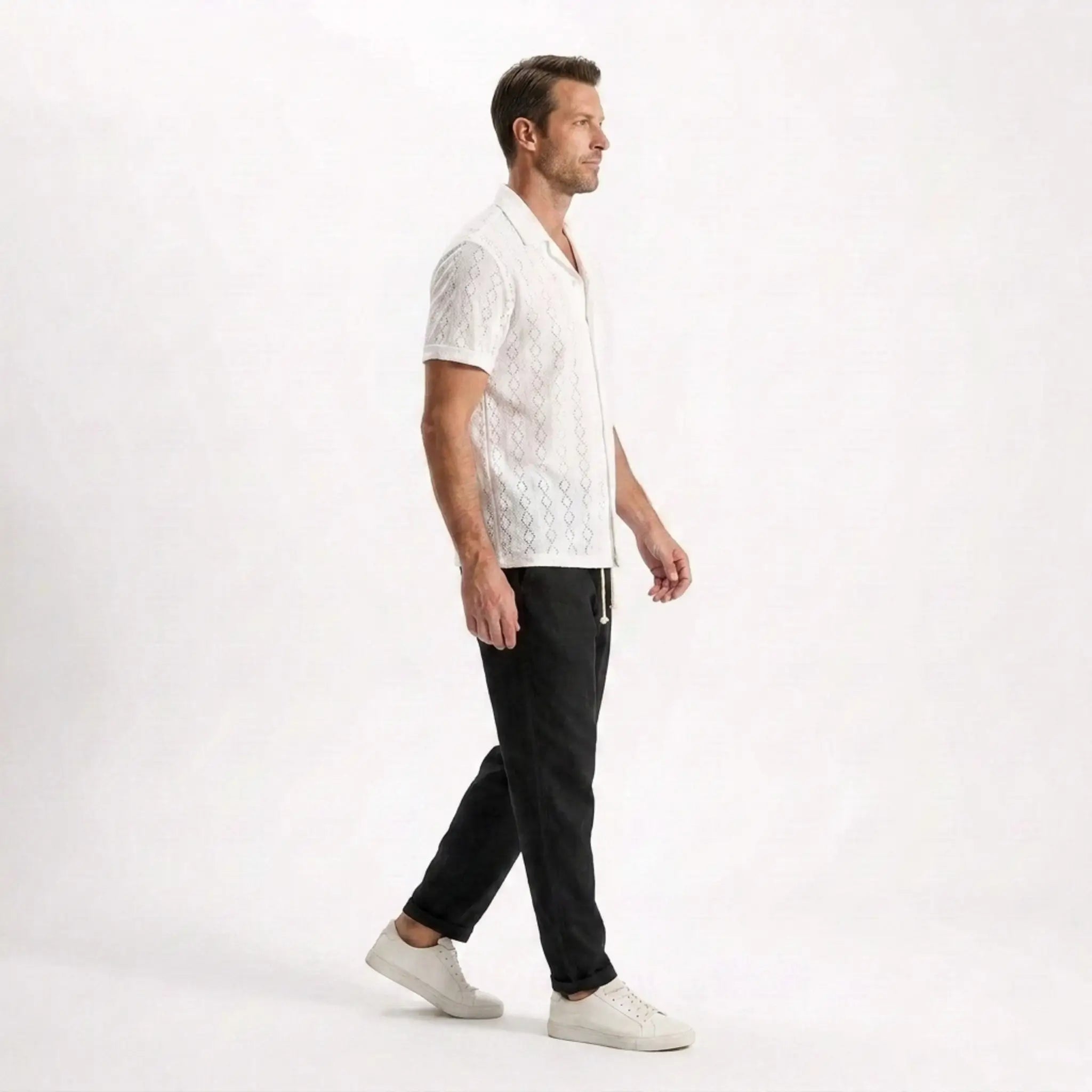 Man wearing a white patterned shirt and black pants on a white background
