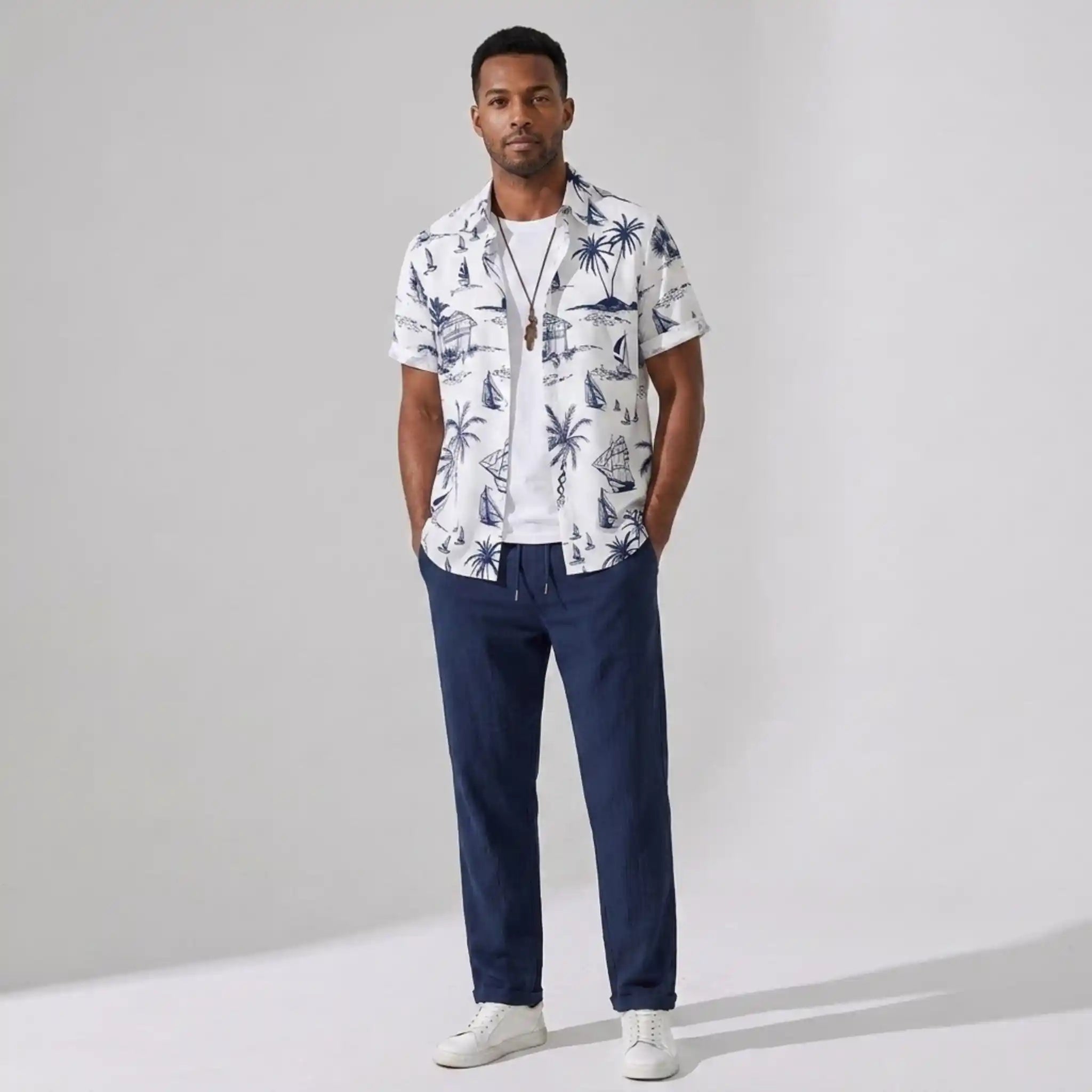 Man wearing a white patterned shirt and navy pants on a gray background