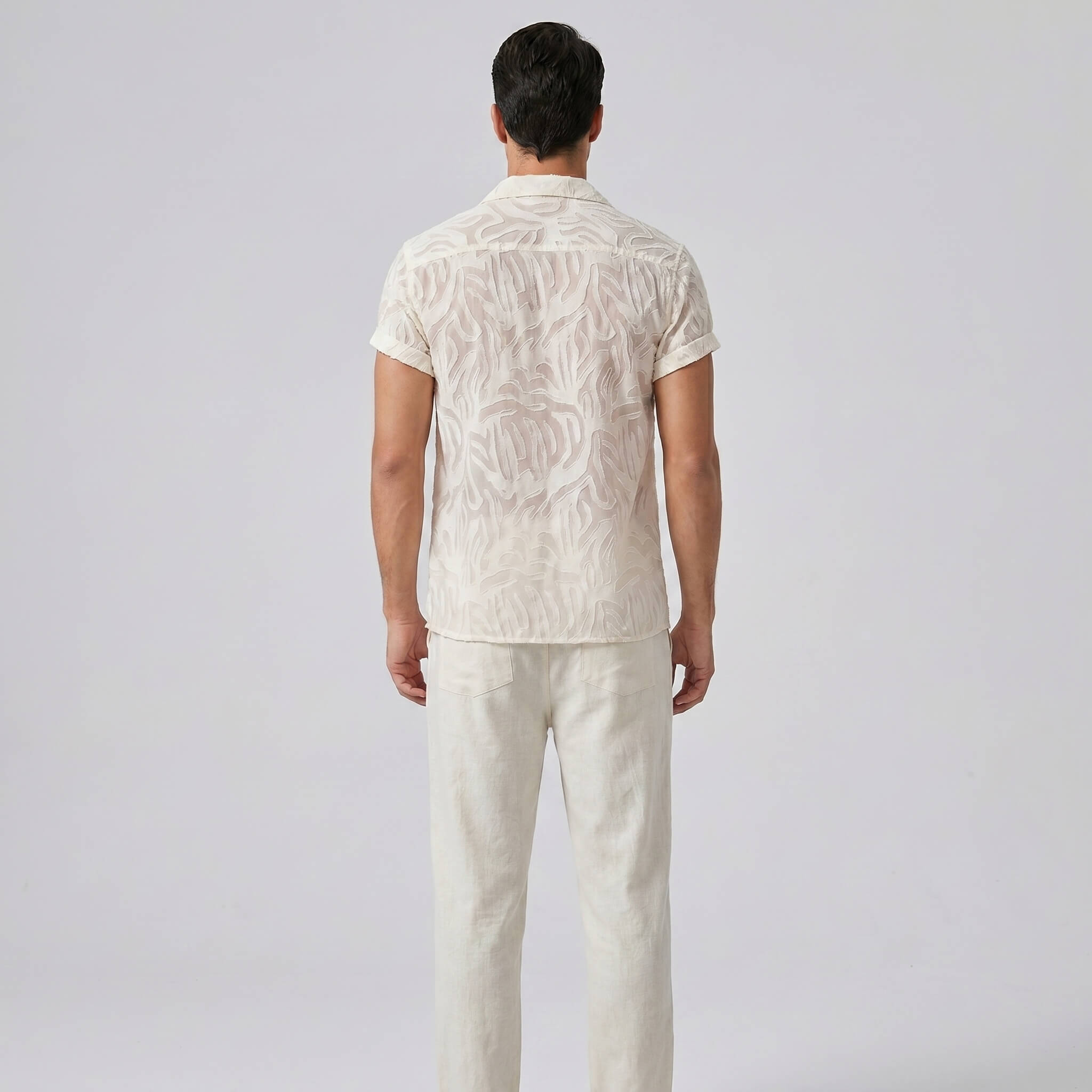 Man wearing a white patterned shirt and pants on a light gray background