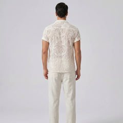 Man wearing a white patterned shirt and pants on a light gray background