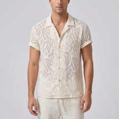 Man wearing a white patterned shirt and pants on a plain background
