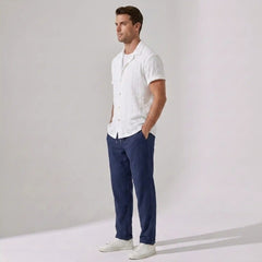 Man wearing a white patterned shirt, navy pants, and white shoes against a plain background