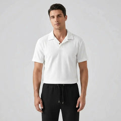 Man wearing a white polo shirt and black pants against a gray background