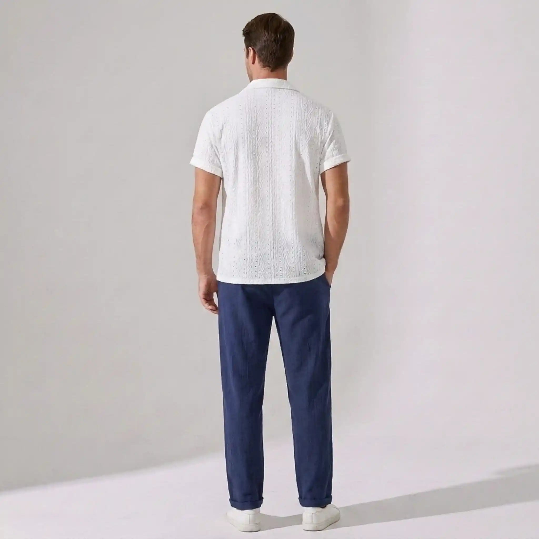 Man wearing a white shirt and blue pants against a plain background