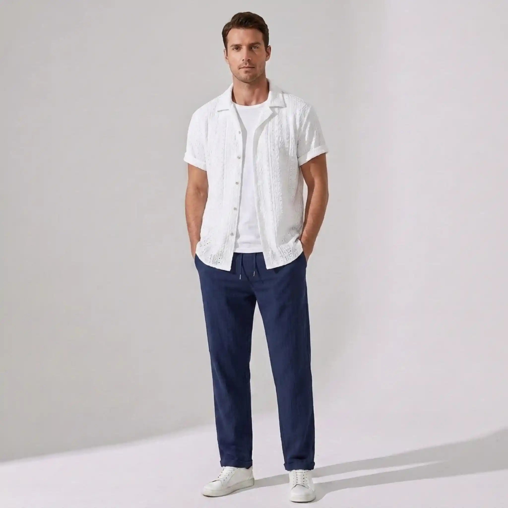 Man wearing a white shirt and navy pants against a plain background