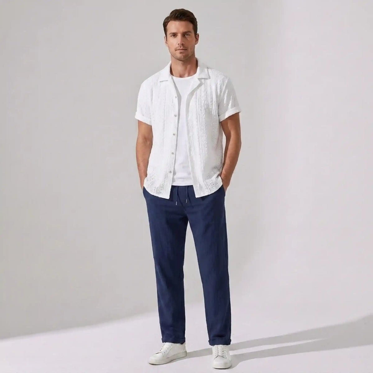 Man wearing a white shirt and navy pants against a plain background