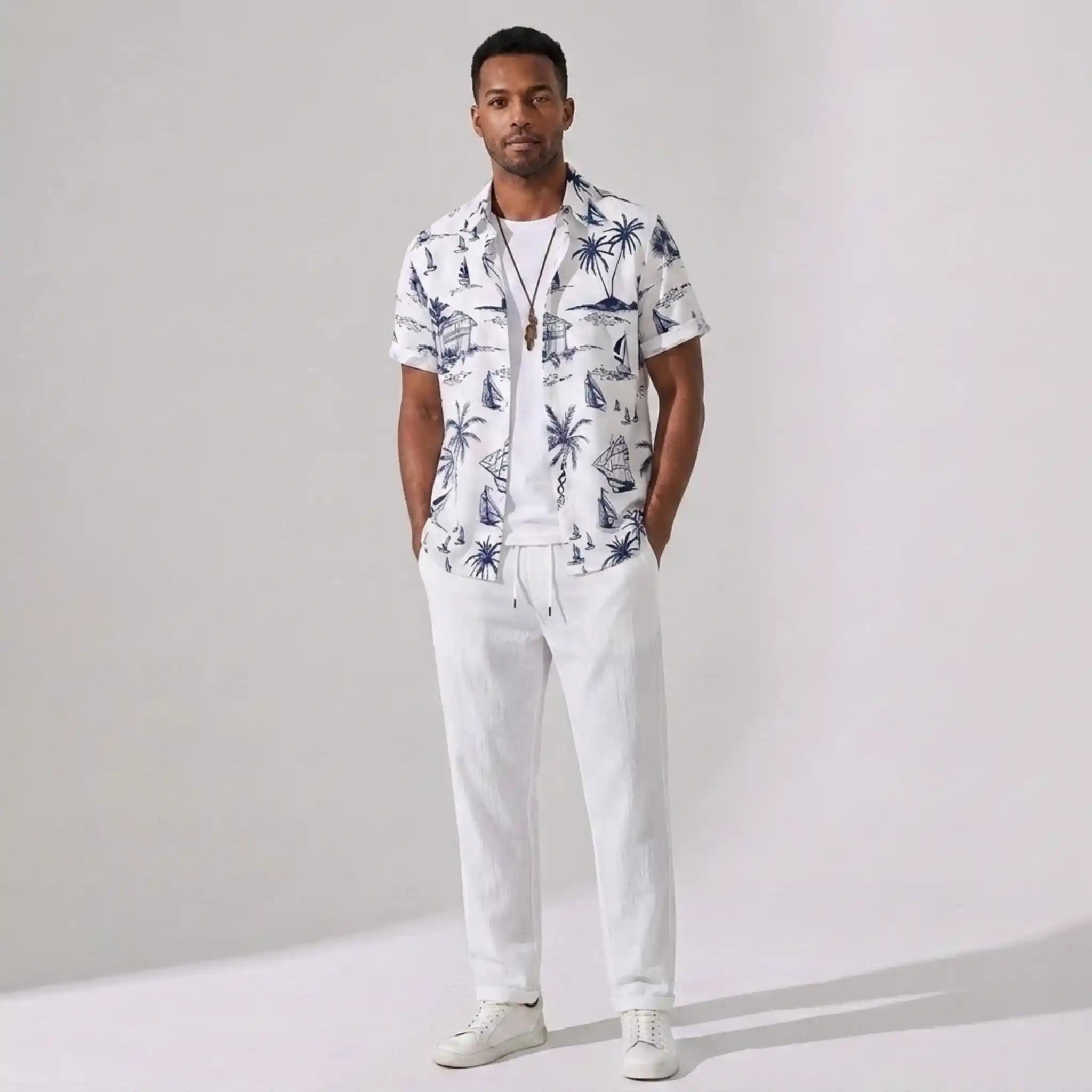 Man wearing a white shirt with a tropical pattern and white pants on a plain background