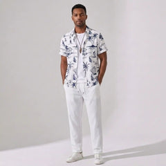 Man wearing a white shirt with a tropical pattern and white pants on a plain background