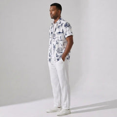 Man wearing a white shirt with blue patterns and white pants against a gray background