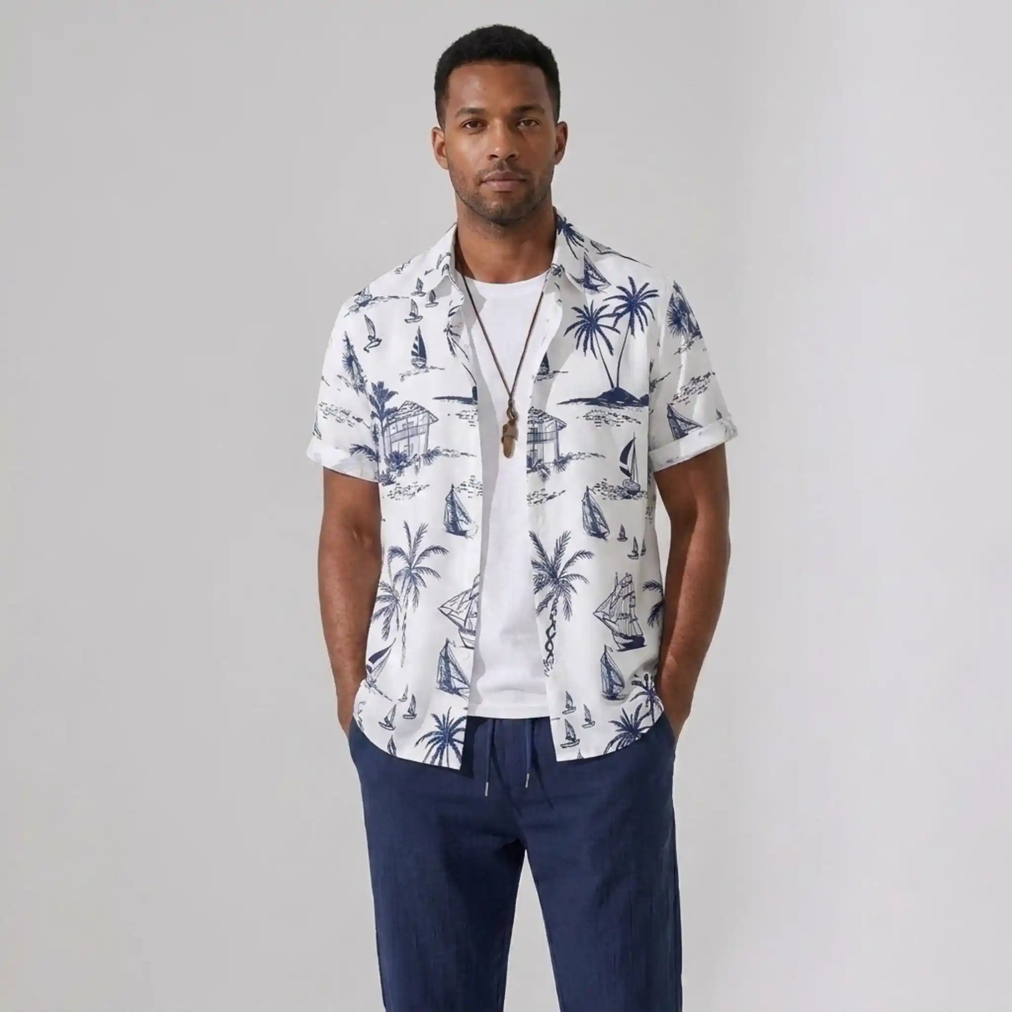 Man wearing a white shirt with blue tropical patterns and navy pants on a gray background