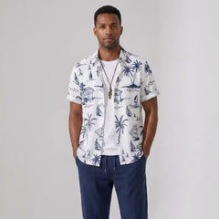 Man wearing a white shirt with blue tropical patterns and navy pants on a gray background