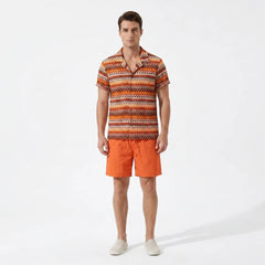 Man wearing an orange patterned shirt and shorts on a white background