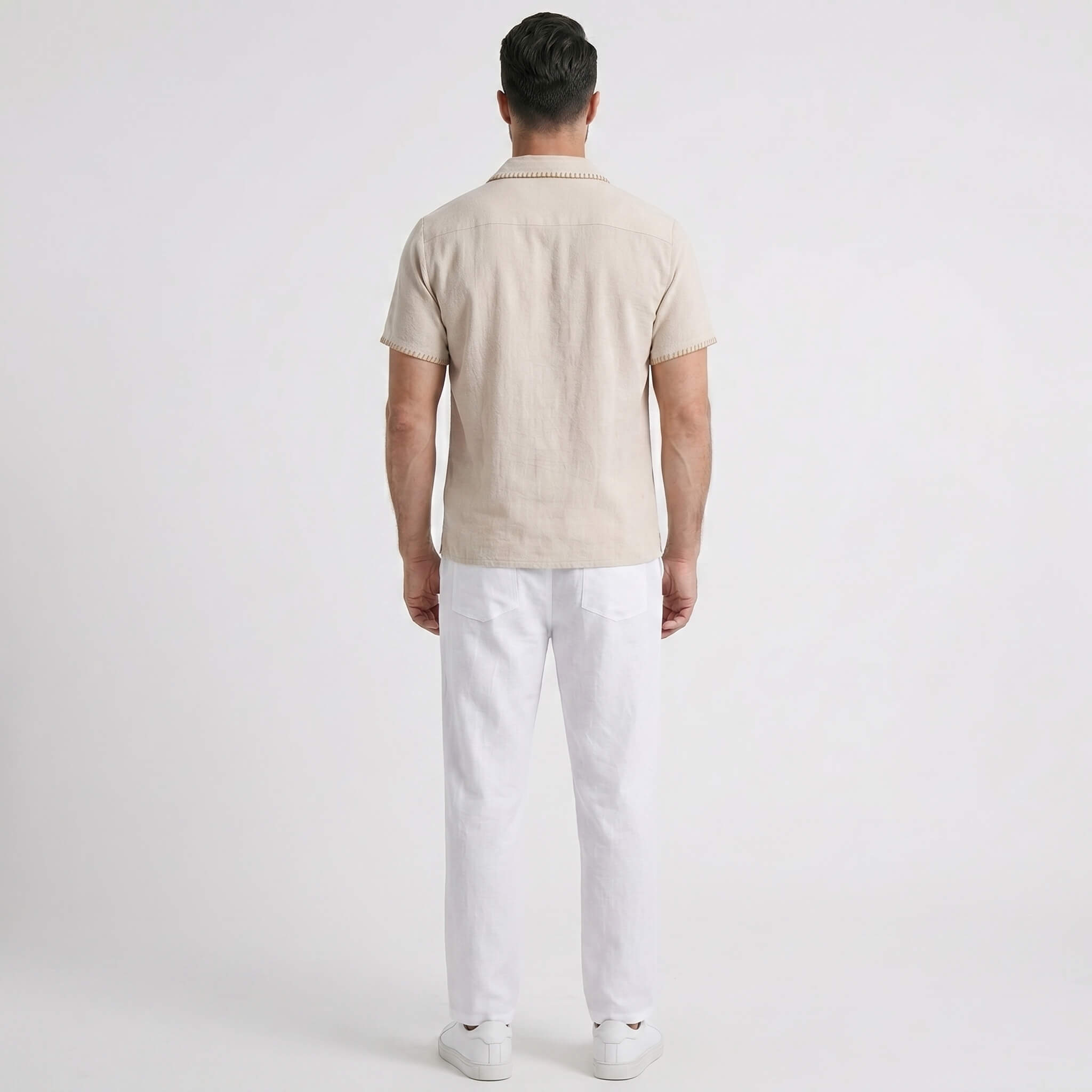 Man wearing a beige short-sleeve shirt and white pants on a light gray background
