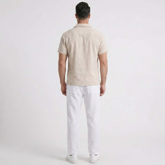Man wearing a beige short-sleeve shirt and white pants on a light gray background