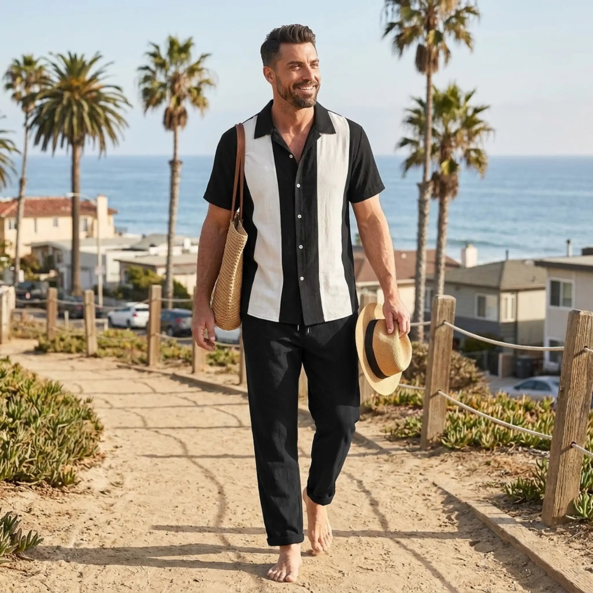 Man wearing black and white strip shirt and black trouser walking along a path by the beach with palm trees and ocean in the background