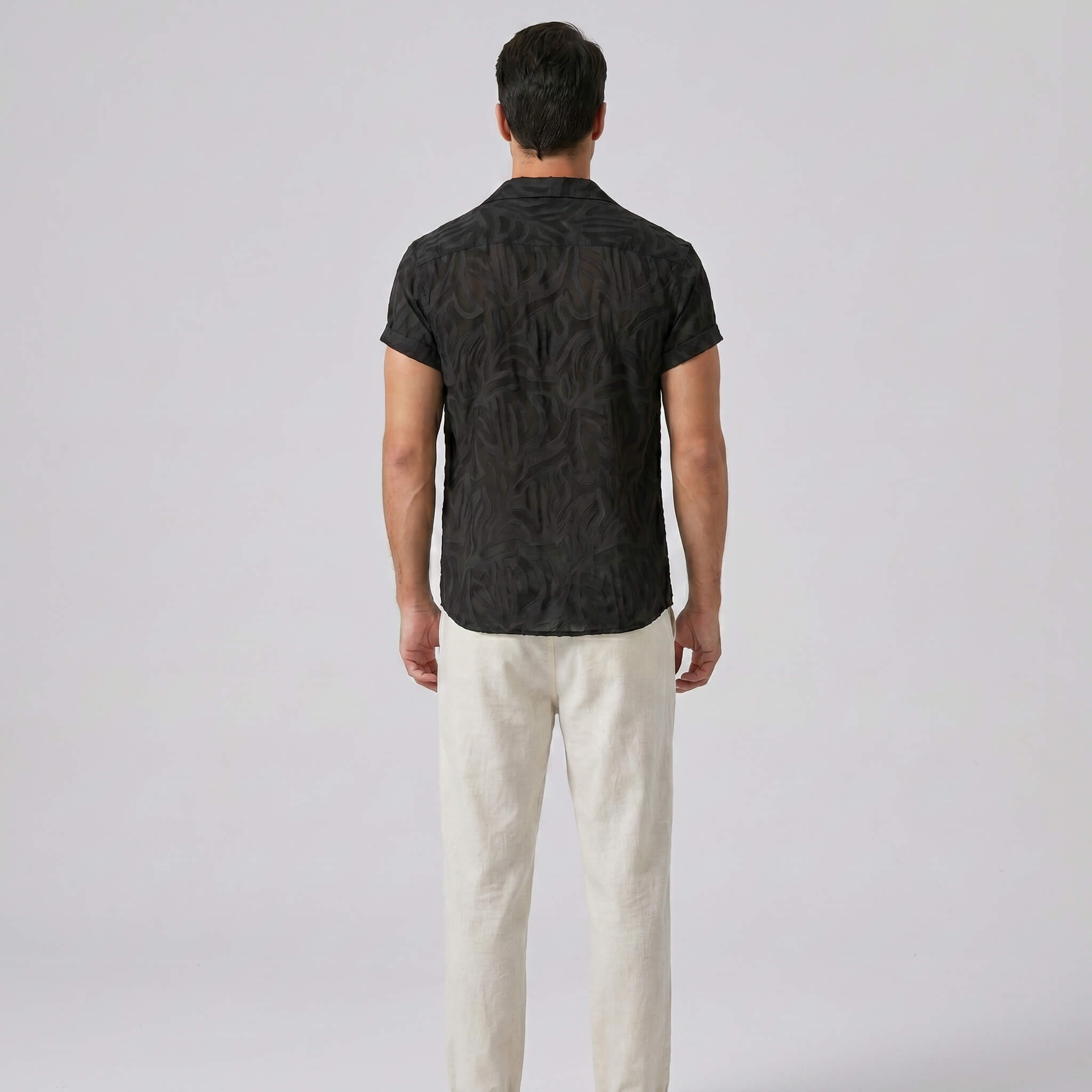 Man wearing a black patterned shirt and white pants on a light gray background