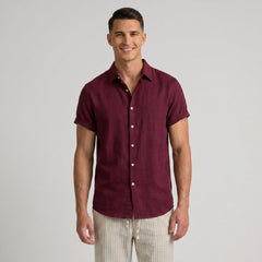 Man wearing a maroon textured polo shirt and white pants on a light gray background