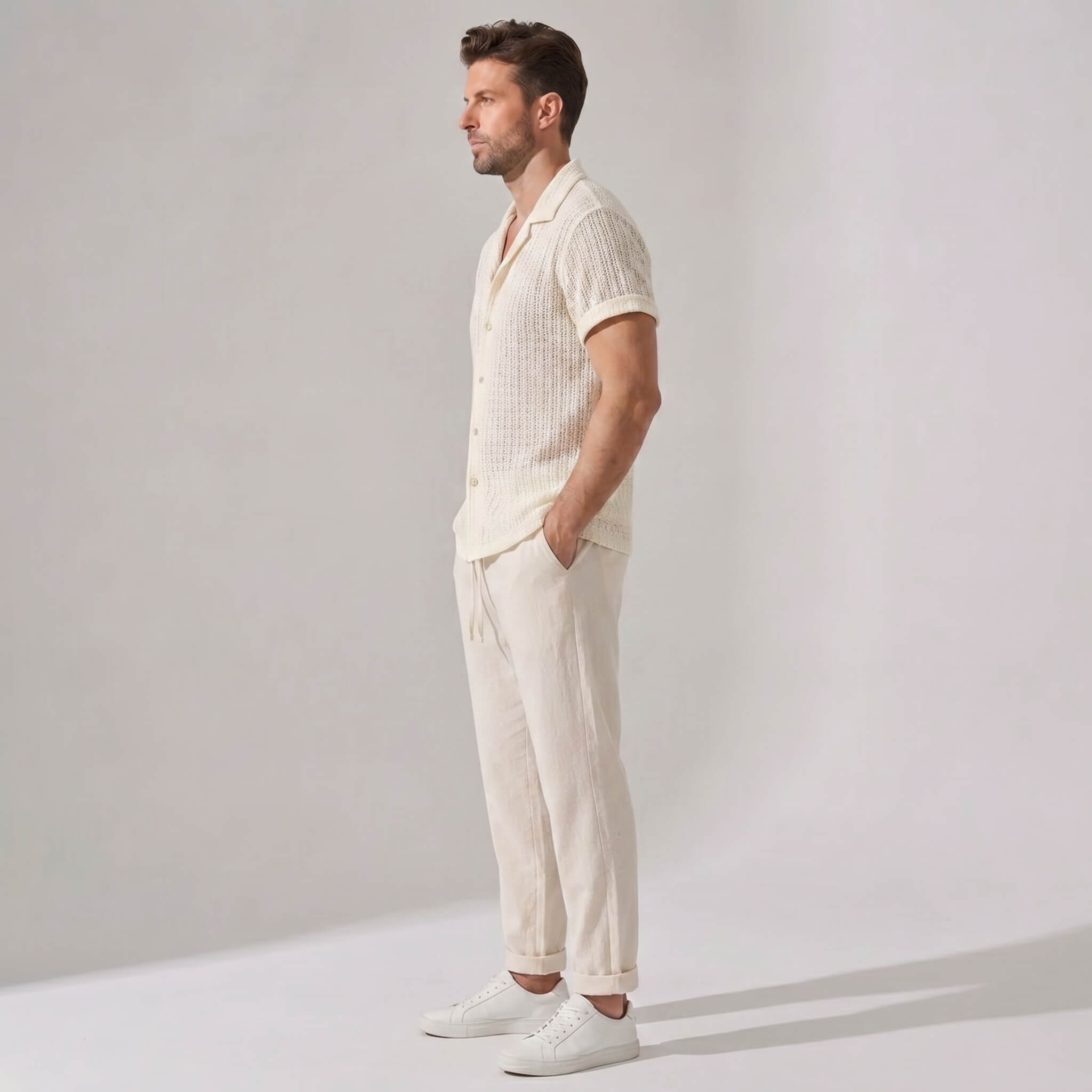 Side view of man wearing a cream-colored outfit with a shirt and pants on a plain background