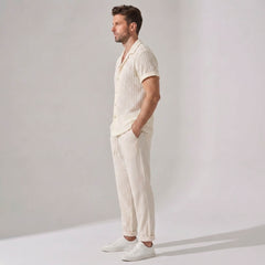 Side view of man wearing a cream-colored outfit with a shirt and pants on a plain background